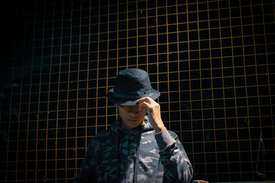 Man in hat standing against fence 