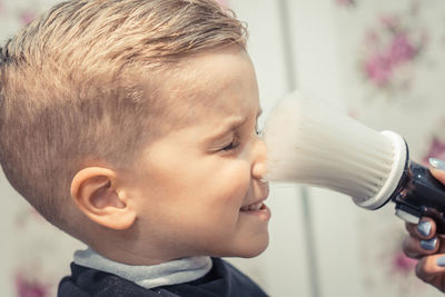 Cropped hand of female hairdresser cleaning boy with brush in salon