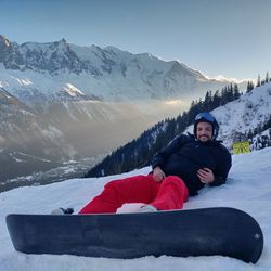 People on man with snowboard reclining on snow against mountains