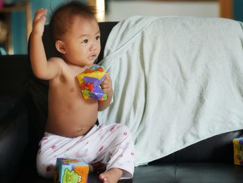 Shirtless boy with toys sitting at home