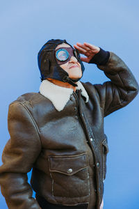 Senior woman wearing glasses while saluting against blue background