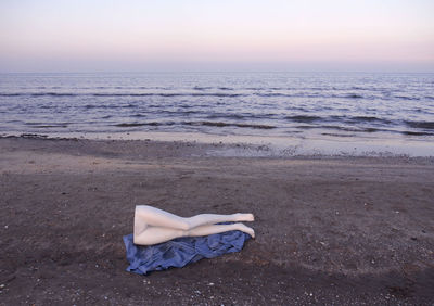 Woman relaxing on beach against sky during sunset