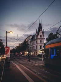 Street amidst railroad tracks in city against sky at dusk