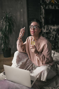 Young woman using phone while sitting on laptop