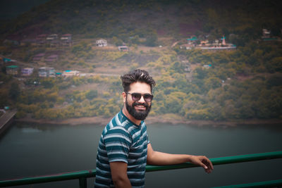 Portrait of young man wearing sunglasses standing against railing