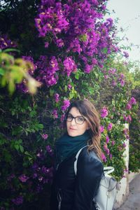 Portrait of beautiful young woman standing by pink flowering plants
