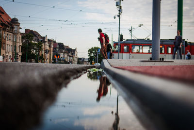 Reflection of people in puddle on street against sky