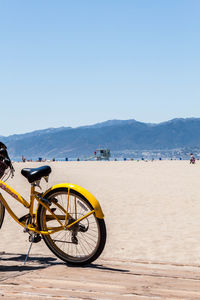 Yellow bicycle at beach against clear sky on sunny day