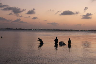 Silhouette men standing on shore against sky during sunset