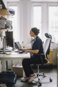 Side view of mature female nurse working on computer while sitting at desk in clinic