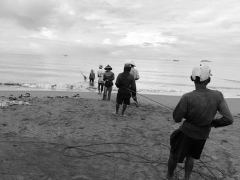 Rear view of men holding rope at beach