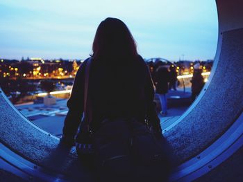 Rear view of mid adult woman sitting against sky at dusk