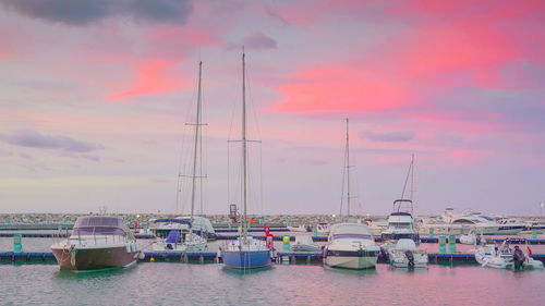 Sailboats moored at harbor against sky during sunset