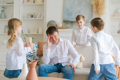 Tired father, sitting on couch in living room, feels annoyed and exhausted