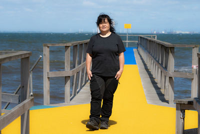 Portrait of teenage girl standing on railing against sea