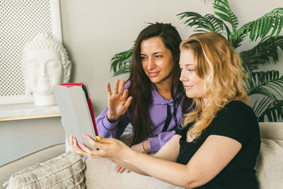 Two girls are sitting on the couch at home and making a video call to friends.