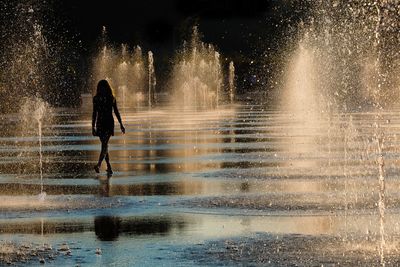 Silhouette of woman in fountain against sky during sunset