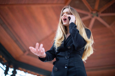 Low angle view of woman using phone standing below gazebo