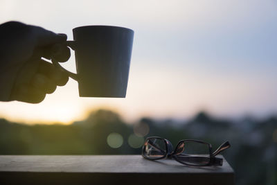 Close-up of hand holding coffee cup against sky