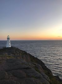 Lighthouse by sea against sky during sunset