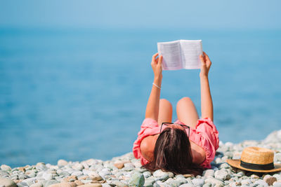 Midsection of woman reading book against sea