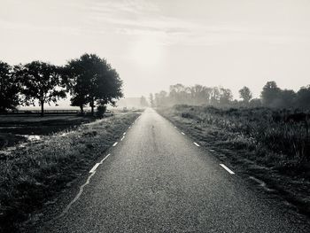 Road amidst trees on field against sky