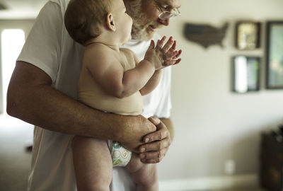 Grandfather carrying shirtless grandson while standing at home