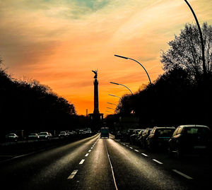Road by silhouette trees against sky at sunset