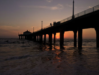 Silhouette bridge over sea against sky during sunset