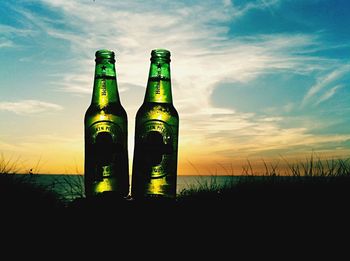 Close-up of beer glass bottle against sky during sunset