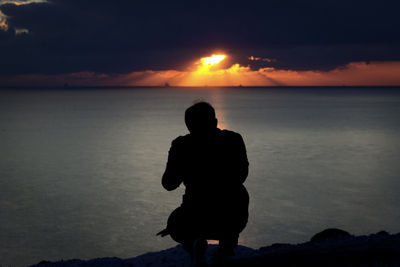 Silhouette man on sea against sky during sunset