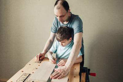 Cute little boy with pencil in hand making marks on wooden plank. father teaches son carpentry