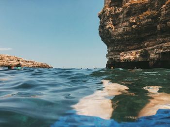 People by rock formation in sea against sky