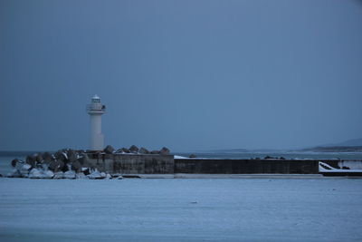 Lighthouse by sea against clear sky