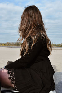 Rear view of woman sitting at beach against sky