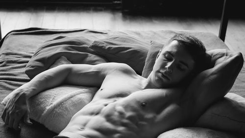 High angle view of shirtless muscular male model lying on bed at home