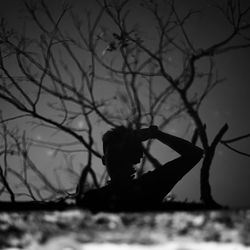 Silhouette woman standing by bare tree against sky