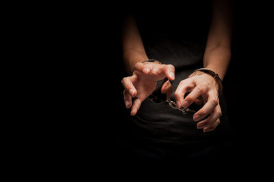 Midsection of woman with handcuffs against black background