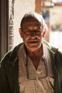 Senior craftsman in casual outfit friendly smiling and looking at camera while standing near entrance of workshop