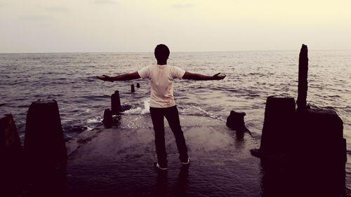 Rear view of man with arms raised on beach