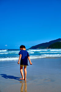 Rear view of man standing on beach against clear sky