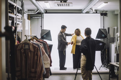 Male design professional measuring jacket by fashion model during photo shoot in studio