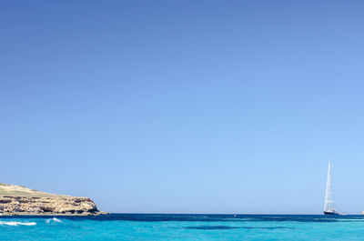 Sailboat sailing in sea against clear blue sky