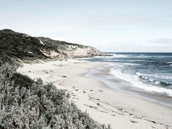 Scenic view of ocean beach with cliffs against sky in light cool tones 