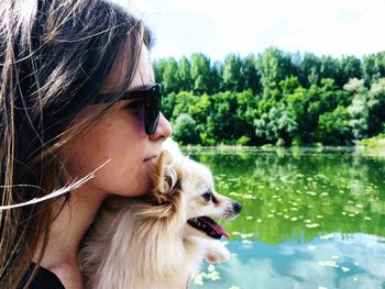 Side view of young woman with dog standing by lake against trees