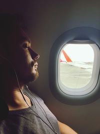 Side view of man looking through airplane window