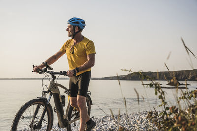 Man wearing cycling helmet walking with bicycle at beach