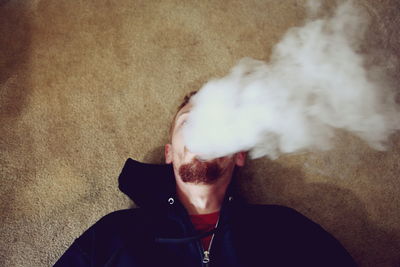 High angle view of man smoking while lying on carpet at home