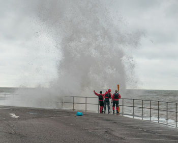Men looking at large wave crashing on railing