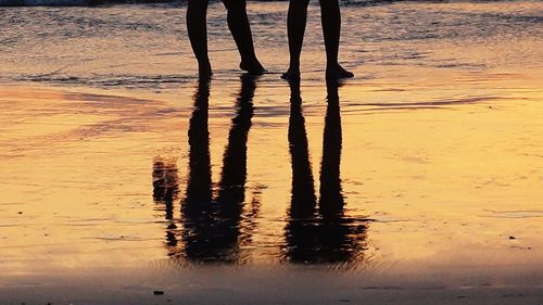 Low section of silhouette people on water at sunset